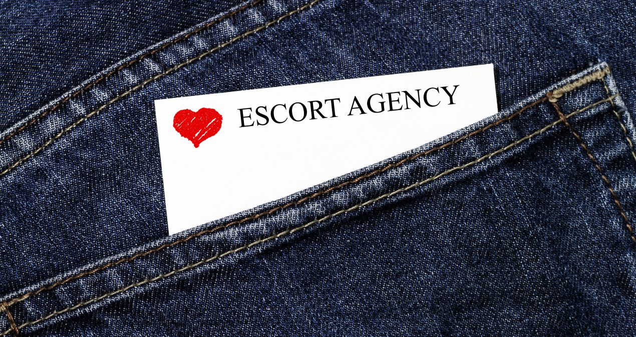 Visitenkarte mit der Aufschrift "Escort Agency" und einem roten Herz, halb sichtbar in der Gesäßtasche einer Jeans.