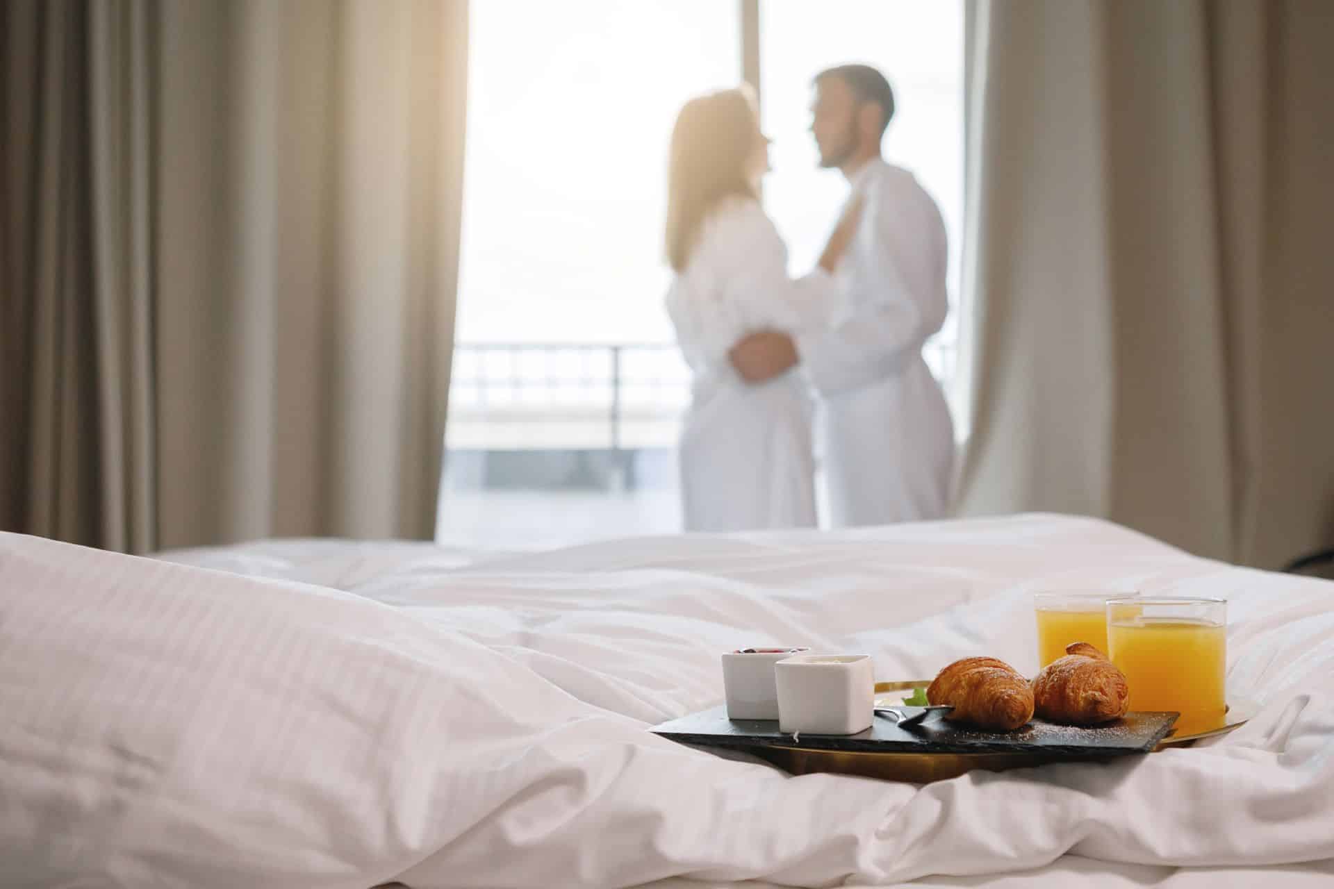 Frühstück auf Hotelbett mit Paar im Hintergrund in Bademänteln